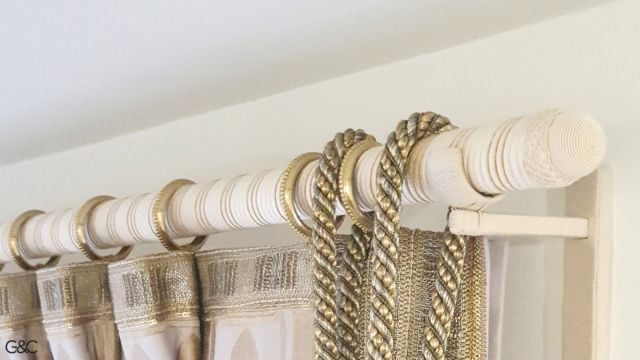 La tringle à rideaux, les embouts et les supports sont ornés de passementerie