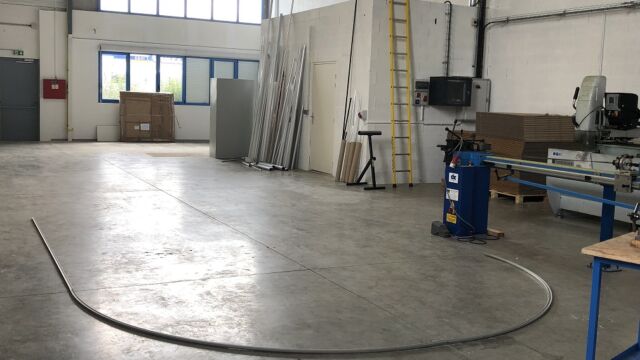 Rail pour stores en ellipse de 25 m de long posé au sol avant le montage dans l’atelier du fabricant français
